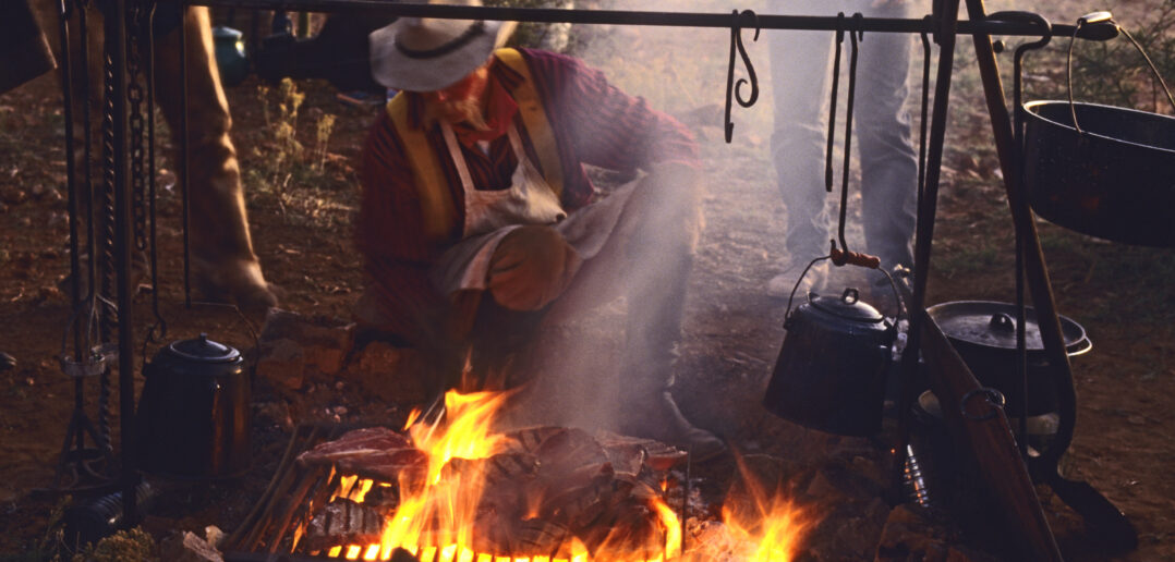 Chuckwagon cook Mike Ryan grills steaks for dinner over an open fire at cowboy camp