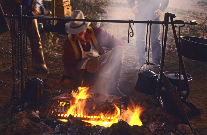 Chuckwagon cook Mike Ryan grills steaks for dinner over an open fire at cowboy camp