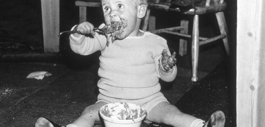 A young child sitting under a table eating Christmas pudding