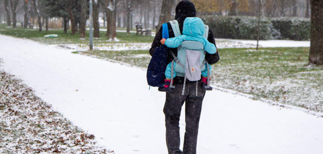 A man with a child in a backpack carrier walks along the Rusanivka embankment as it snows
