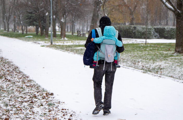 A man with a child in a backpack carrier walks along the Rusanivka embankment as it snows