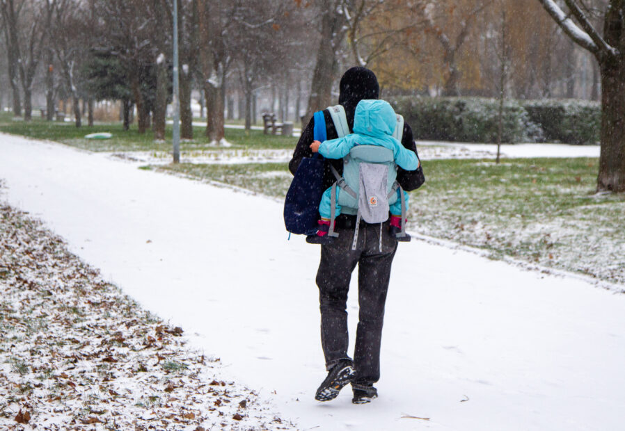 A man with a child in a backpack carrier walks along the Rusanivka embankment as it snows